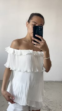 Balta off-the-shoulder palaidinė su klostuota tekstūra ir volaniniu kaklu. Pasižymi laisvu siluetu ir sluoksniuota dizainu. Minkšta medžiaga.