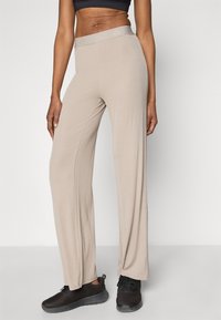 Beiget leveälahkeiset housut, joissa pehmeä kangas ja joustava vyötärönauha, yhdistetty mustiin urheilukenkiin. Yksinkertainen muotoilu ja rento istuvuus.