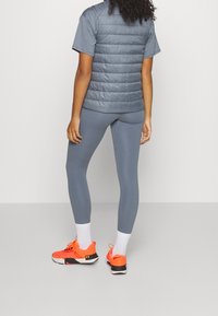Gray puffer vest over a gray t-shirt, paired with gray leggings and bright orange sneakers. White socks visible above the sneakers.