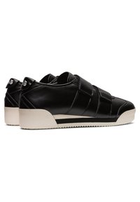 Paire de baskets en cuir noir à coupe basse avec semelles blanches et deux bandes velcro ajustables, vues de côté et de dos.