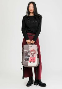 Der Rucksack hat gemischte Muster mit Illustrationen, hauptsächlich in Grau mit roten Akzenten. Aus Textilmaterial, rechteckige Form, verstellbare Riemen.