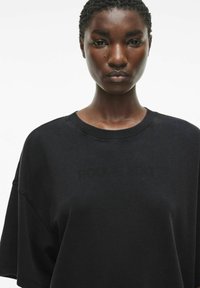 Sudadera negra de gran tamaño con cuello redondo. Textura suave y corte holgado, con un sutil logo impreso en la parte delantera.