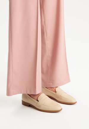 Mocassini in pelle beige con finitura testurizzata e fascia decorativa, abbinati a pantaloni a gamba larga rosa chiaro.