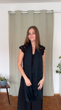 Μαύρο, ελαφρύ κασκόλ γύρω από το λαιμό· απαλής υφής με λείο φινίρισμα. Στο φόντο υπάρχει μπεζ κουρτίνα και ένα φυτό.