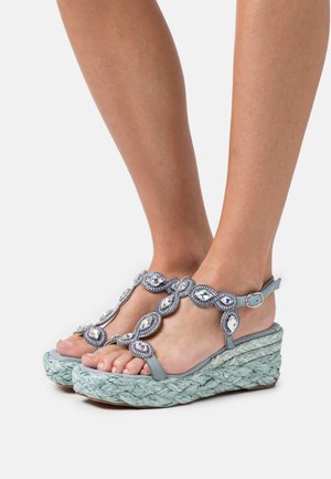Sandales compensées bleu clair avec une semelle en jute tressé, des brides ornées de strass et une fermeture à boucle.