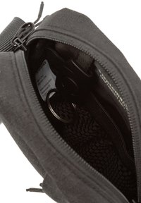 Offene schwarze Tasche mit einem Netzinnenteil und einem Metallschlüsselring darin. Ein Etikett ist an der Seite sichtbar.