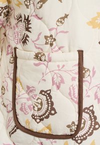 Gewatteerd stoffen jas met een bloemenpatroon in roze, geel en bruin, met een bruin afgewerkte zak en een zachte, gestructureerde oppervlakte.