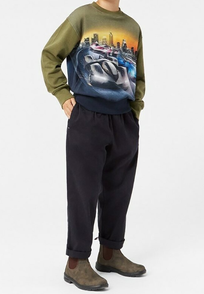 Grafická mikina s gradientem od olivově zelené po námořnickou, s potiskem městské krajiny a vozidel; doplněná černými širokými kalhotami a hnědými botami.