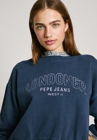 Mörkblå sweatshirt med rundad hals, oversize-passform och texten "LONDONER PEPE JEANS WEST 11" i vitt. Mjukt bomullstyg.