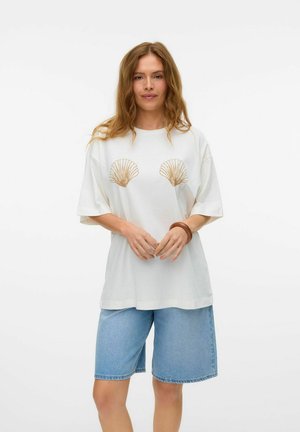 Biały T-shirt z krótkim rękawem z złotymi nadrukami muszelek na klatce piersiowej, w połączeniu z jasnoniebieskimi szortami dżinsowymi o luźnym kroju.