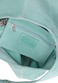 Sac à main en cuir vert menthe, avec un compartiment principal et une poche zippée. L'intérieur présente une texture lisse et une étiquette "Fabriqué en Italie".