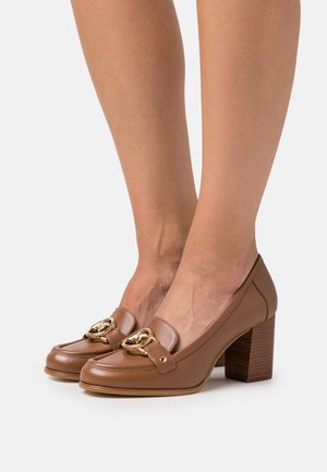 Mocassins à talons en cuir marron avec un accent de chaîne dorée, bout arrondi et talon bloc texturé effet bois. Finition lisse avec détails de couture.
