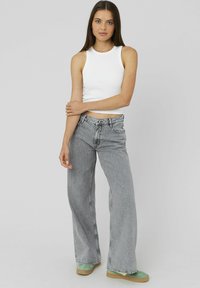 Jean large gris associé à un débardeur blanc ajusté. Les jeans ont une taille haute et un délavage léger, complétés par des chaussures vertes.