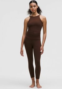 Brown athletic set featuring a sleeveless crop top and high-waisted leggings. The fabric has a smooth, stretchy texture with seamless design.