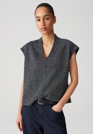Top grigio texturizzato con maniche corte a cappuccio e scollatura a V, abbinato a jeans scuri. Il tessuto presenta un motivo sottile per un tocco di dettaglio in più.