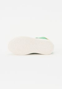 Groene schoen met een geëxtrudeerde rubberen zool, voorzien van groeven en cirkels voor grip. Glad materiaal met een minimalistisch ontwerp en een contrasterende hak.