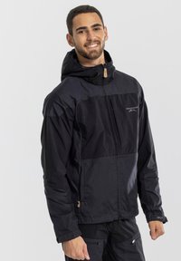 Giacca nera con cappuccio caratterizzata da una chiusura zip frontale, design con pannelli a contrasto e polsini regolabili. Il materiale sembra leggero e resistente.