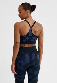 Marinblå sportbh med geometrisk mönster och racerback-design. Har strukturerad tyg och justerbara axelremmar för perfekt passform och stöd.