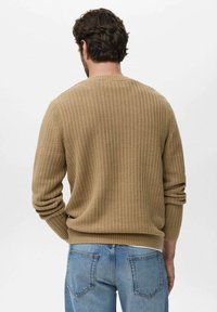Beige gebreide trui met ribbeltextuur en lange mouwen, met een ronde halslijn en een aansluitende tailleband, gedragen over blauwe jeans.