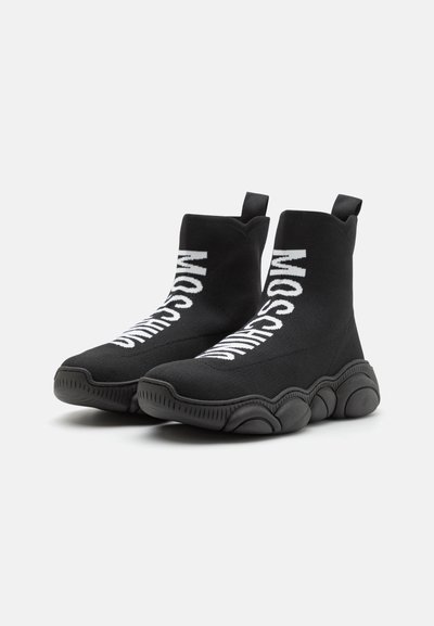 Black knitted ankle boots with a chunky sole. Features bold white branding on the sides and pull tabs on the back for easy wear.