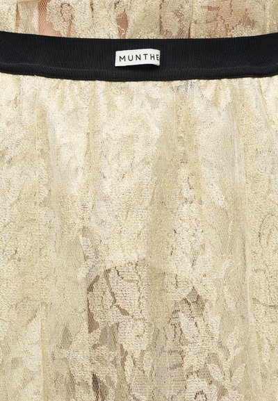 Φούστα από δαντέλα σε λαμπερό χρυσό με μαύρη ελαστική μέση. Διαθέτει ανθικά σχέδια και διαφανές, υφασμάτινο φινίρισμα. Εταιρική ετικέτα: MUNTHE.