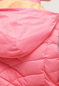Rosa pufferjacka med kviltad textur, med en stor huva och ett orangefärgat foder. Hållbart, lätt material.