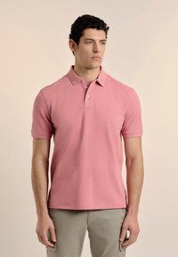 Camisa polo de manga corta en color rosa, confeccionada en tejido de algodón texturizado, con un cuello de dos botones y un pequeño logo en el pecho.