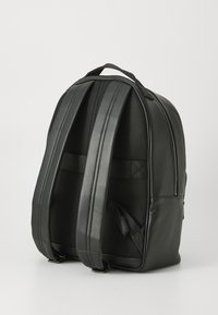 Mochila negra de cuero con correas de hombro acolchadas, panel trasero de malla y un asa superior sobre un fondo blanco.