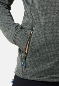 Giacca texturizzata verde scuro con colletto alto, dotata di una tasca laterale con zip e un piccolo accento della bandiera svedese.