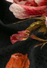 Tkanina s kvetinovým vzorom v čiernej farbe, s odtieňmi ružových, červených a oranžových ruží. Mäkčená textura so zvrásneným vzhľadom.