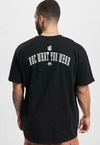 Black cotton t-shirt featuring a round neckline and short sleeves. Text on the back reads "ROC WHAT YOU WEAR -99-" in white.