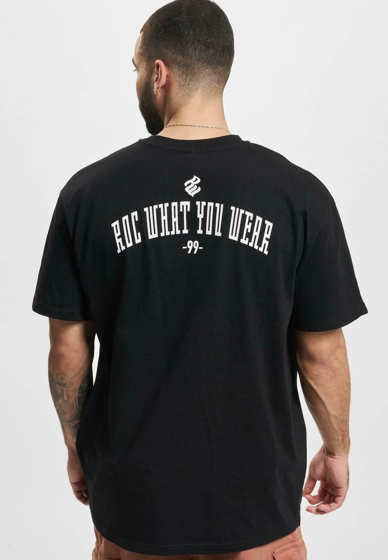 Black cotton t-shirt featuring a round neckline and short sleeves. Text on the back reads "ROC WHAT YOU WEAR -99-" in white.