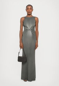 Gray sleeveless maxi dress with a knotted waist detail, smooth texture, paired with a small black handbag, and black open-toe shoes.