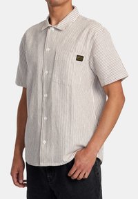 Short-sleeve shirt with a white base and red vertical stripes, featuring a front pocket and branded label, made of lightweight fabric.
