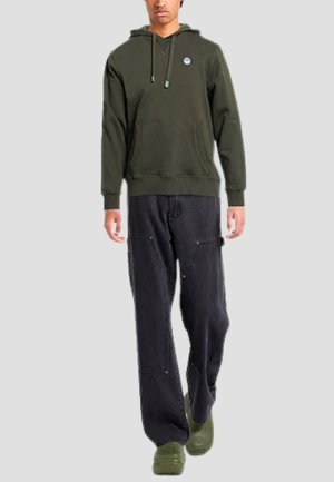 Felpa verde scuro con tasca frontale e coulisse regolabili; abbinata a pantaloni neri larghi e zoccoli verdi. Design semplice e casual.