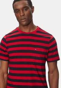 T-shirt a righe rosse e blu realizzato in cotone. Presenta una scollatura rotonda, maniche corte e un piccolo logo sulla tasca del petto.