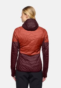 Giacca imbottita in arancione e borgogna scuro, con cappuccio, texture trapuntata e pannelli a contrasto per calore e stile.