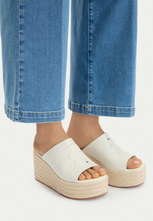 Füße, die weiße Lederkeilsandalen mit offenem Zehenbereich und Sohlen mit Seiltextur sowie kurze blaue Jeans tragen.