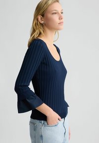 Námořnická modrá ribbed top s dlouhými rukávy, kulatým výstřihem a volánkovými manžetami; má přiléhavý střih a texturovanou látku.