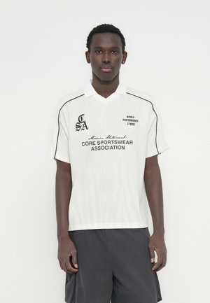 T-shirt de sport blanc avec accents noirs, manches courtes et col en V, portant le texte "WORLD PERFORMANCE STUDIO" et un motif en forme de vague.