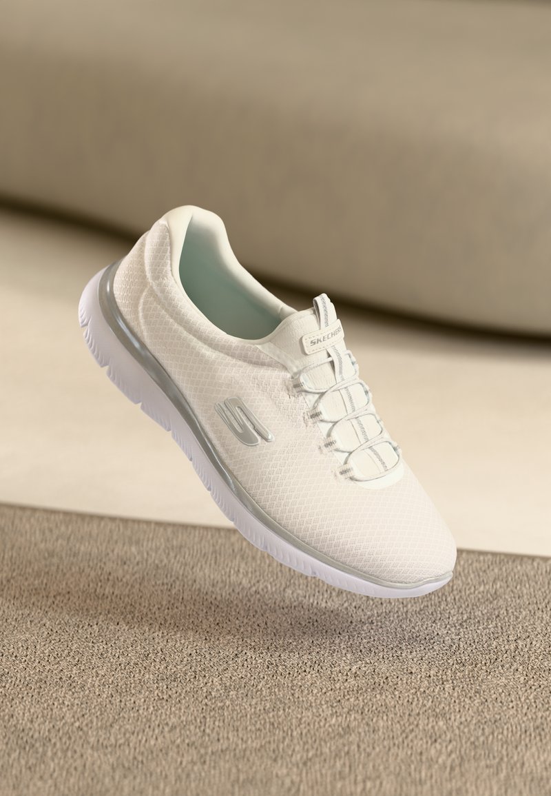 Sneaker bianco in rete con superficie testurizzata, interno azzurro chiaro e suola in gomma bianca. Include un laccio intricato e un dettaglio del logo laterale.