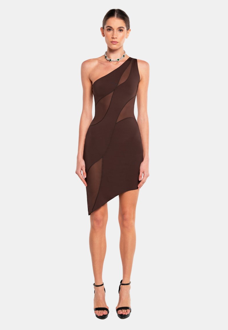 Robe asymétrique marron avec des panneaux transparents, design ajusté et une seule bretelle. Portée avec des escarpins noirs à bride de cheville.