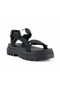 Černá sandal na masivní podrážce s nastavitelnými širokými popruhy a kovovou přezkou na bílém pozadí.
