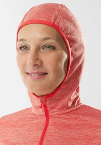 Indumento rosso lavorato a maglia con cappuccio e colletto alto, caratterizzato da un tessuto testurizzato e una zip frontale. Materiale morbido ed elastico, adatto per il freddo.