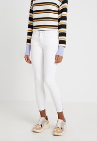 Jeans skinny blancos con cremallera en los tobillos, combinados con un suéter corto a rayas en blanco y negro y zapatillas deportivas gruesas multicolores.