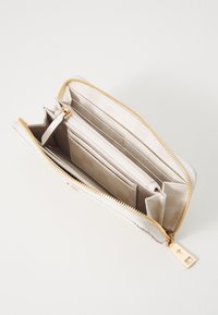 Carteira com fecho em material texturizado bege claro, com acessórios em tom dourado, compartimentos interiores para cartões, dinheiro e um bolso para moedas.