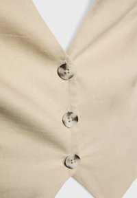 Beżowa lniana kamizelka z głębokim dekoltem w kształcie litery V i czterema okrągłymi, beżowymi guzikami. Tkanina ma gładką fakturę i minimalnie widoczne przeszycia.