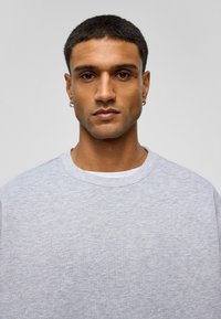 Grijze ronde hals sweatshirt in een zachte, gestructureerde stof, met korte mouwen en een relaxte pasvorm, gedragen over een wit shirt.