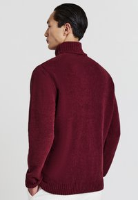 Bordeaux gestrickter Pullover mit hohem Kragen, strukturierter Stoff, gerippte Bündchen und Saum, mit lockerer Passform und subtiler horizontaler Musterung.