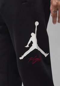 Černé tepláky s velkým bílým logem Jumpman a červeným nápisem "Flight". Vyrobené z měkké látky s přiléhavým střihem.